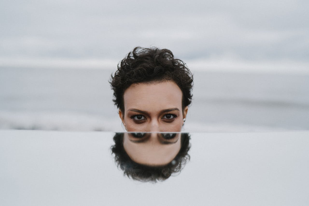 services-02 A moody portrait of a person reflected in a mirror with the ocean as a backdrop.